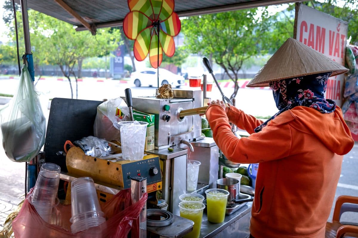A street vendor wearing a conical hat pressing sugarcane juice in Vietnam