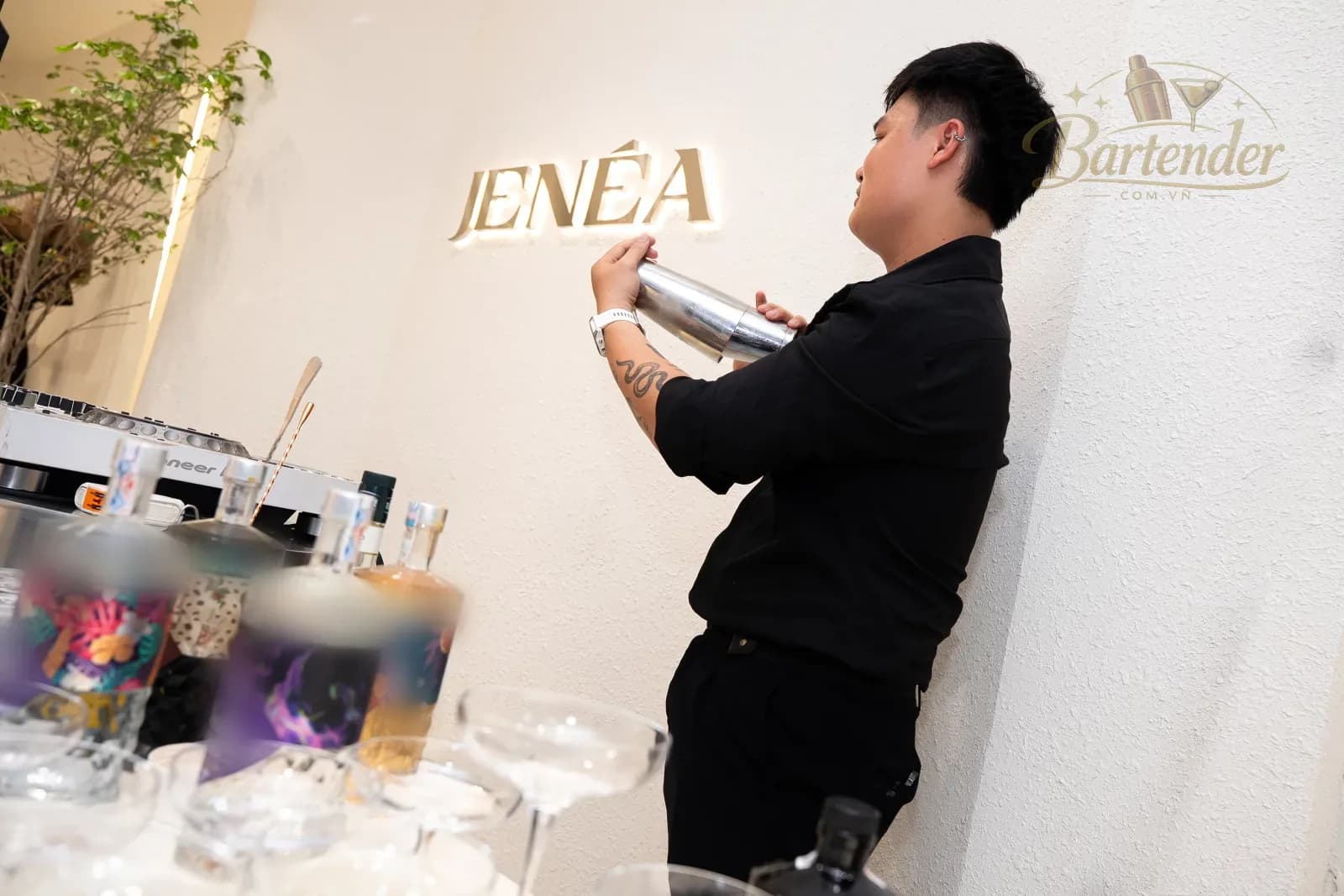 Bartender shaking a drink beneath the Jenéa signage